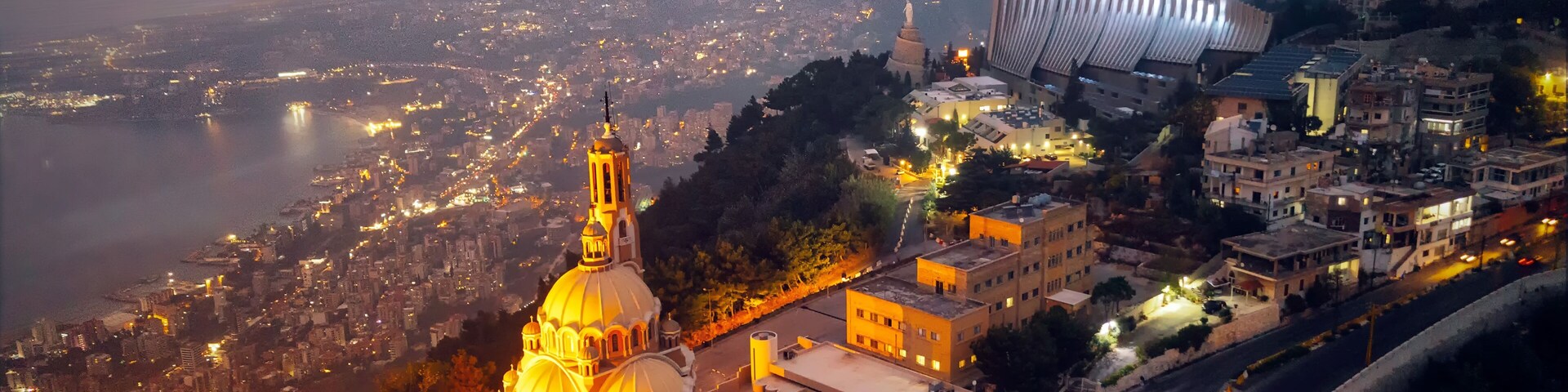 Un paisaje urbano al anochecer con una catedral destacada, un edificio moderno con un techo singular y un río en el fondo.