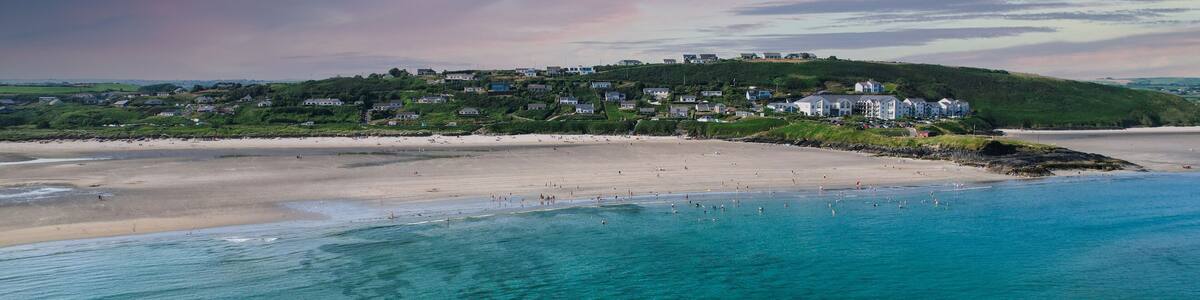 A coastal town with a beach, clear turquoise waters, and a hill with buildings.