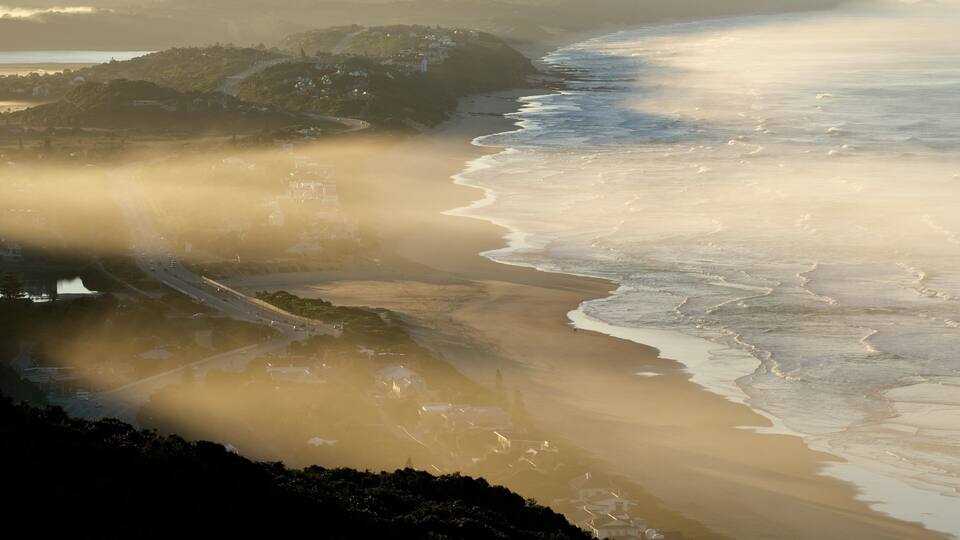 A coastal landscape with a winding road, beach, and buildings on a hillside.