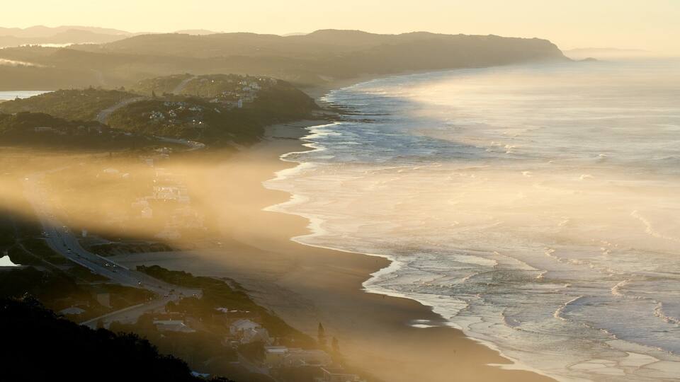 A coastal landscape with a beach, ocean waves, and a road leading to a settlement.
