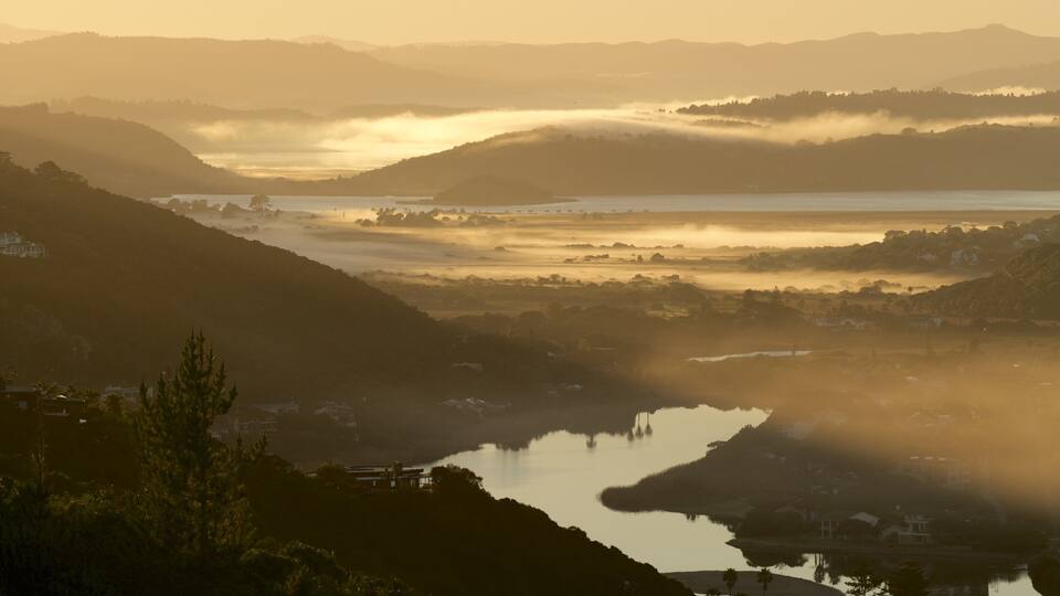 A valley with a lake surrounded by hills and mist.