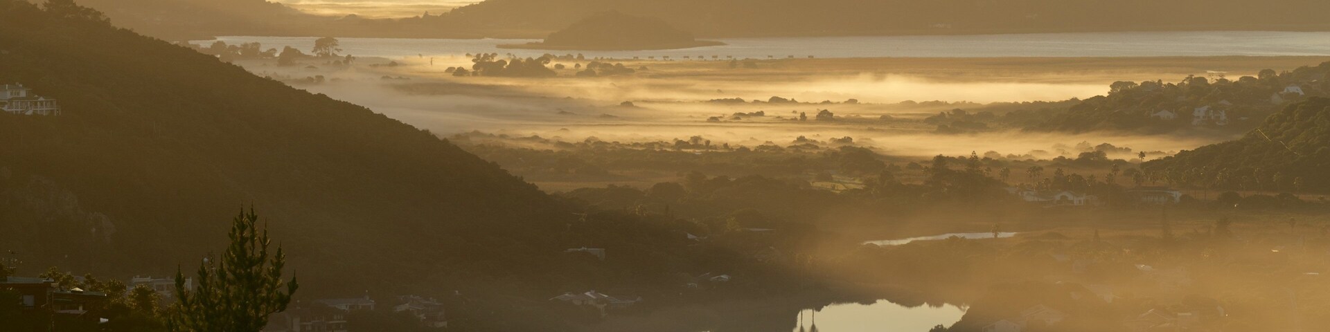 Un valle con un lago rodeado de colinas y neblina.