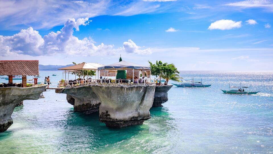 A pier extending over clear turquoise waters, with a covered seating area and boats nearby.