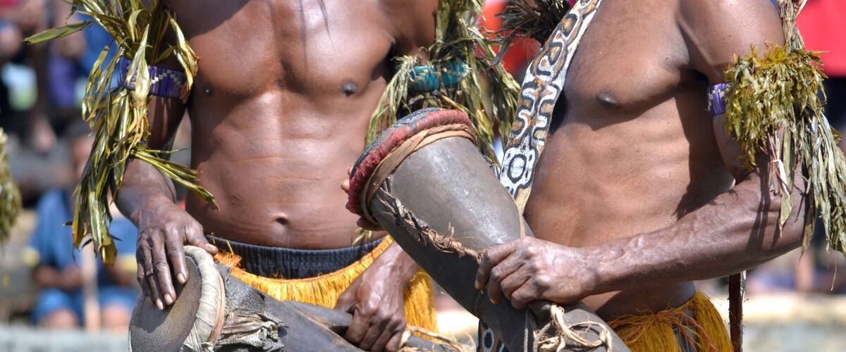 Two individuals in traditional attire holding ceremonial objects.