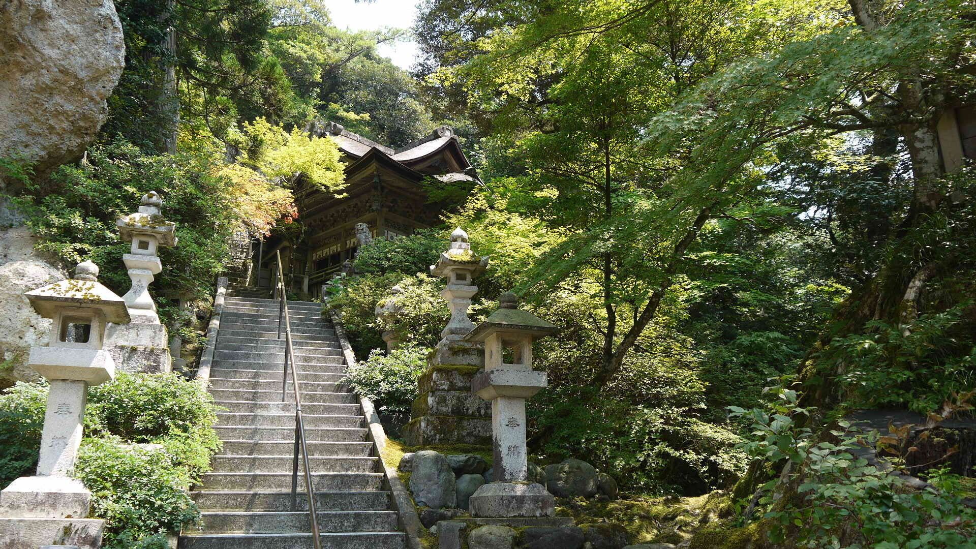 A stone staircase leading up to a traditional Japanese temple surrounded by lush greenery.
