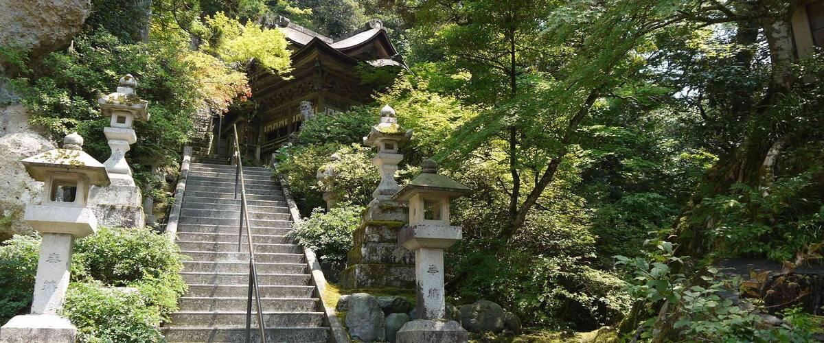 A stone staircase leading up to a traditional Japanese temple surrounded by lush greenery.
