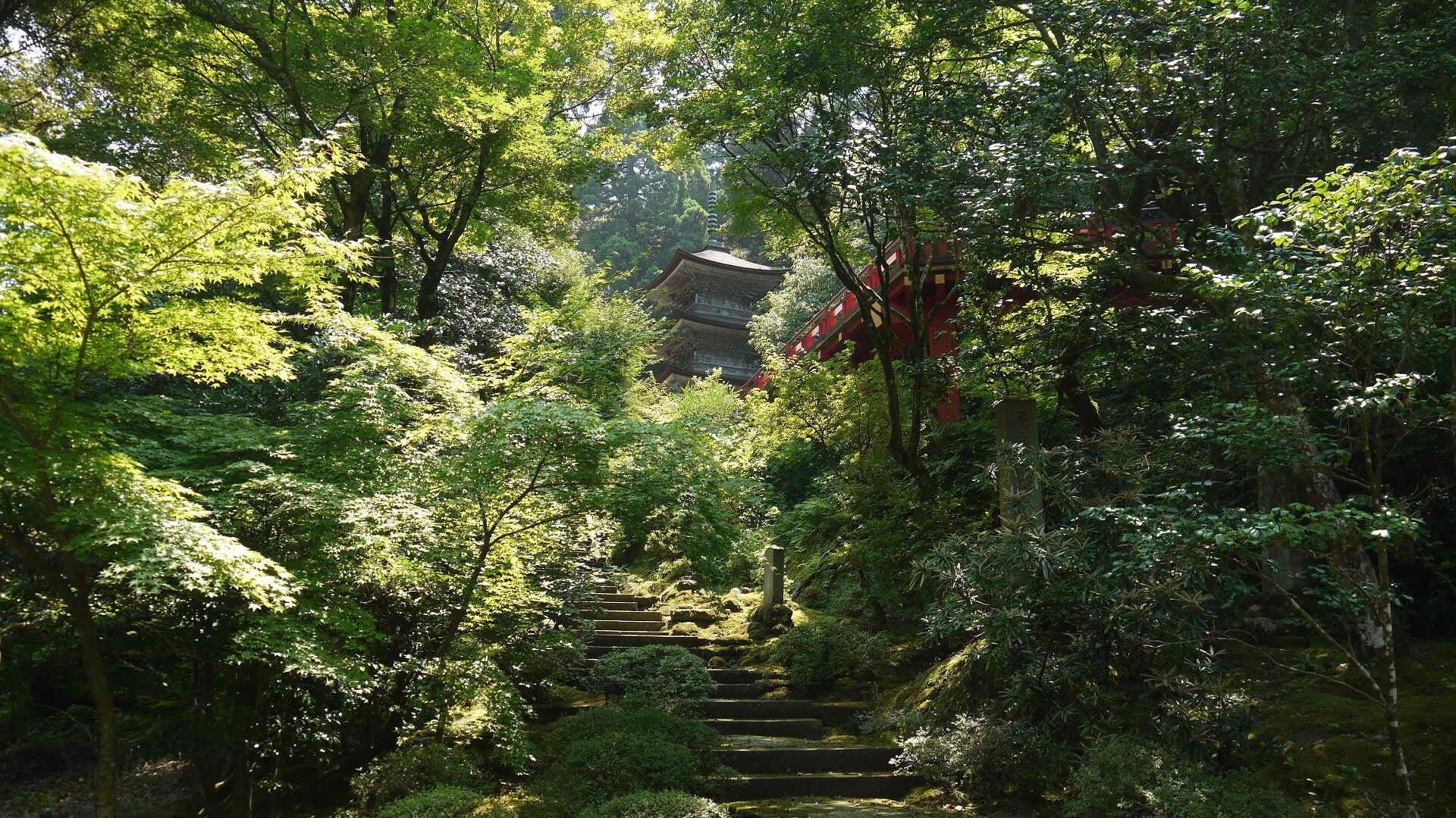 A traditional Japanese pagoda surrounded by lush greenery and a stone staircase leading up to it.