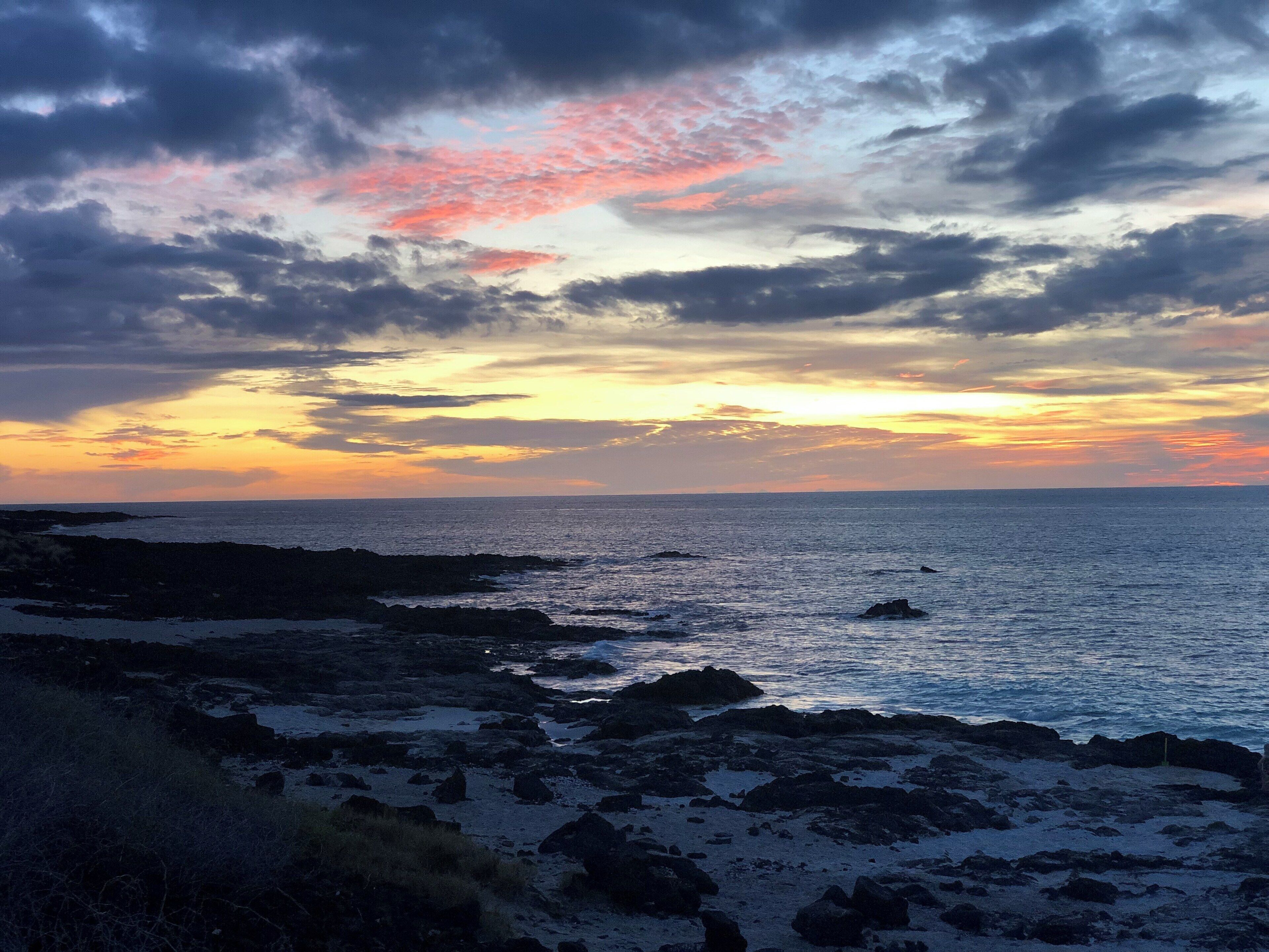 A rocky shoreline with a sunset over the ocean.