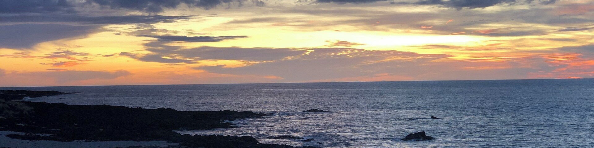 Una costa rocosa con un atardecer sobre el océano.