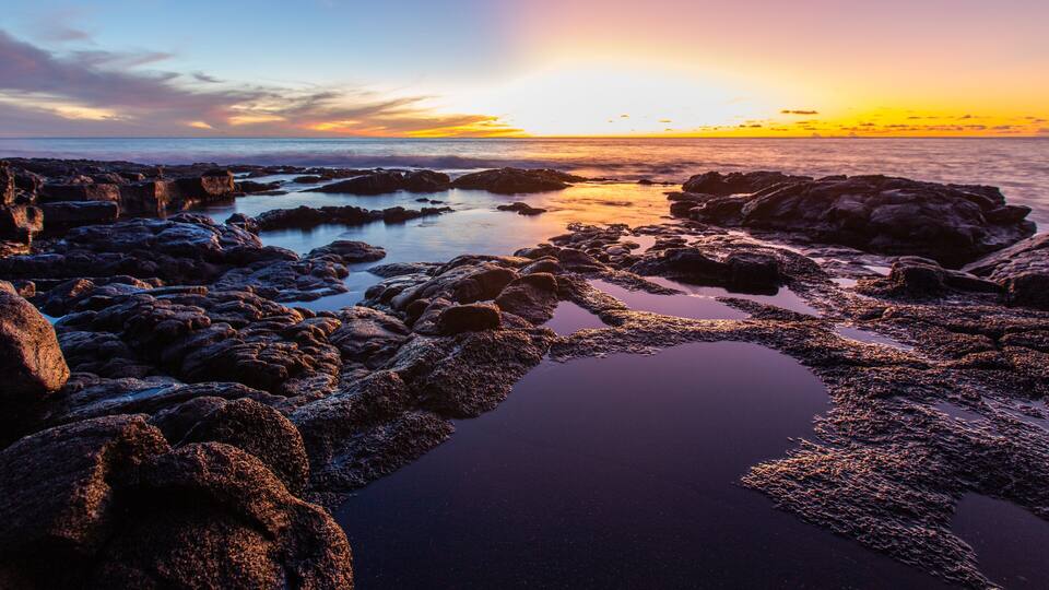 A rocky shoreline with water pools at sunset.