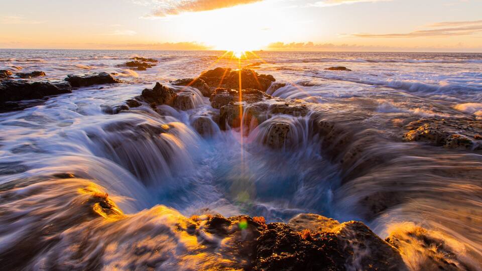 A sunset over a rocky coastline with waves crashing against the rocks.