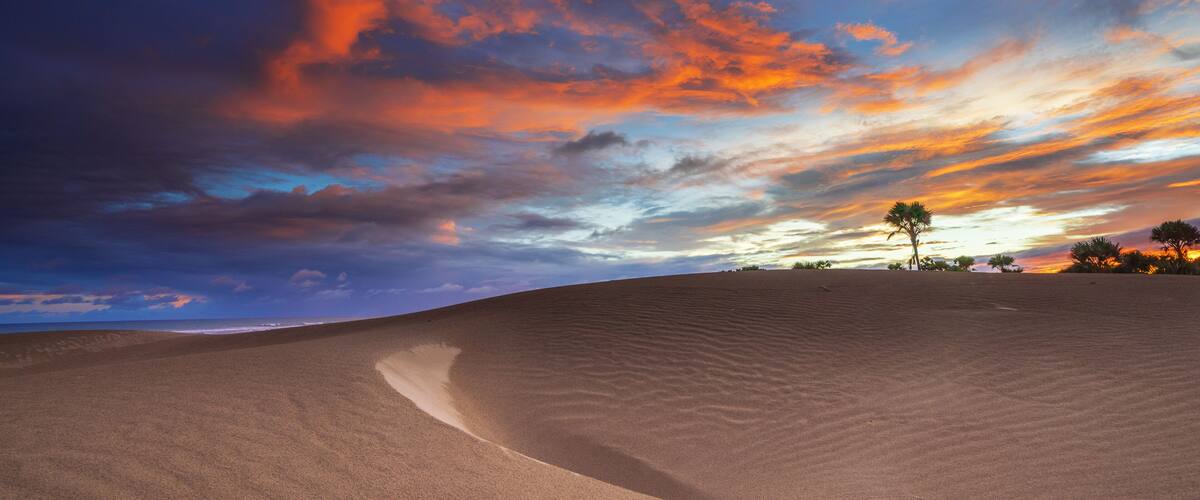 A desert landscape with sand dunes and a sunset sky.