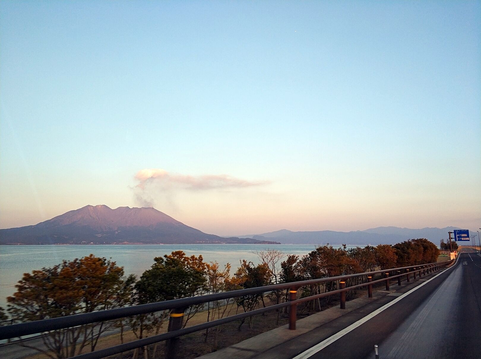 A coastal road with a mountain in the background and a clear sky.