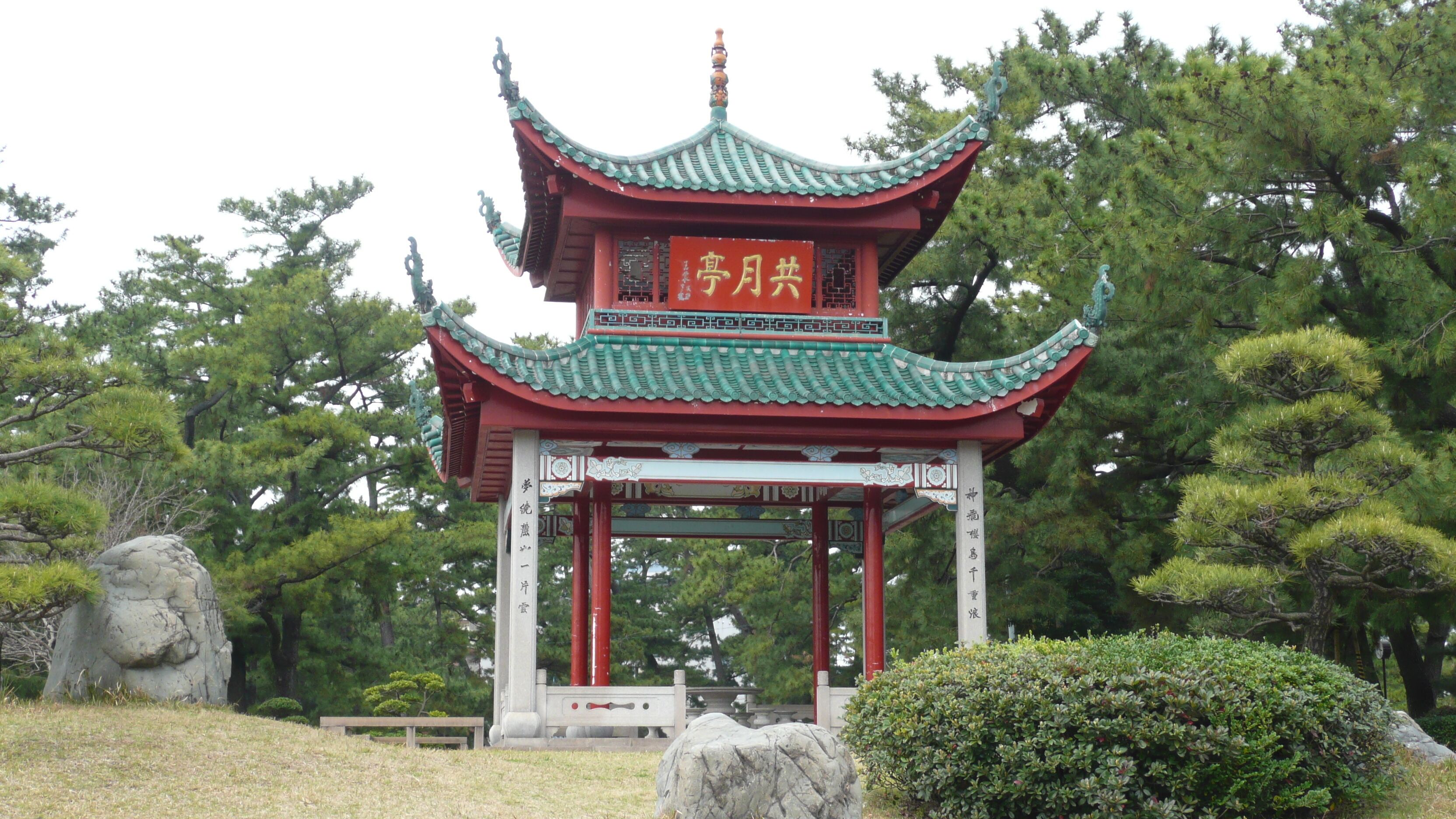 A traditional Chinese pavilion with green and red colors, surrounded by trees and rocks.