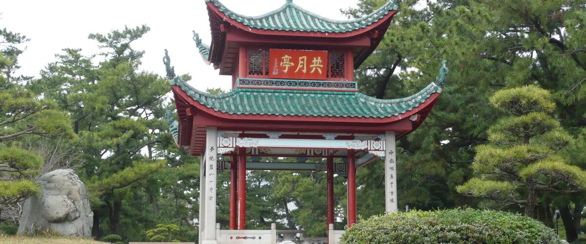 A traditional Chinese pavilion with green and red colors, surrounded by trees and rocks.