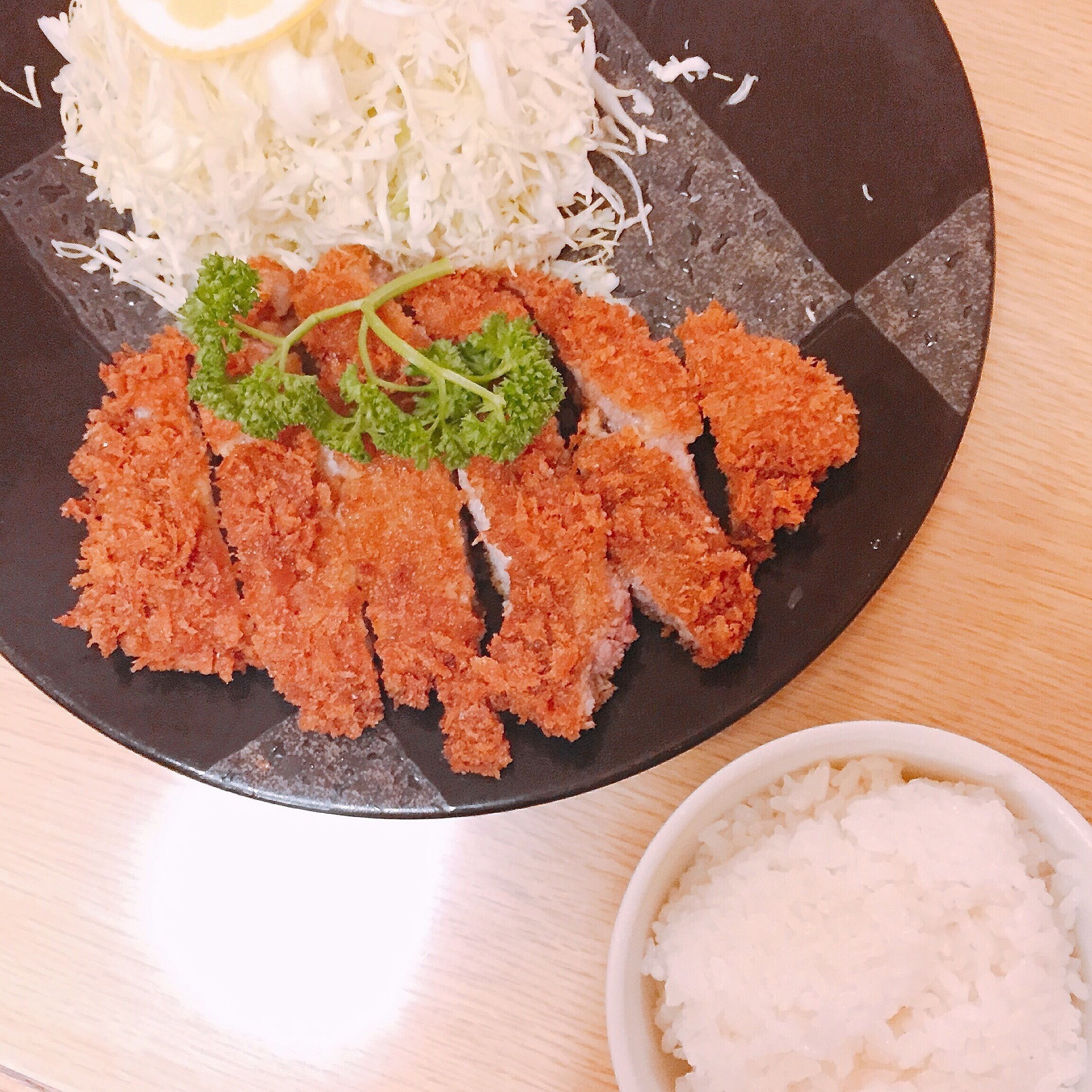 A plate of breaded and fried food, possibly chicken, with shredded cabbage and a small bowl of rice.