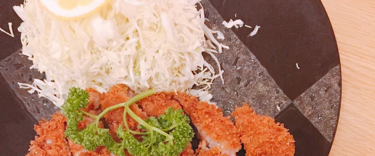 A plate of breaded and fried food, possibly chicken, with shredded cabbage and a small bowl of rice.
