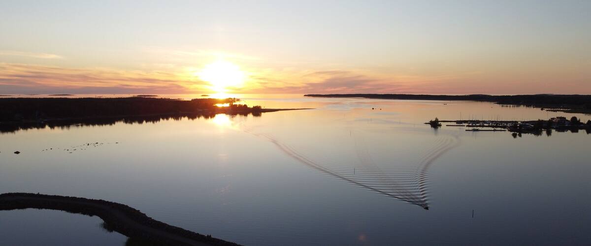 A sunset over a calm lake with a boat wake, shoreline, and distant land.