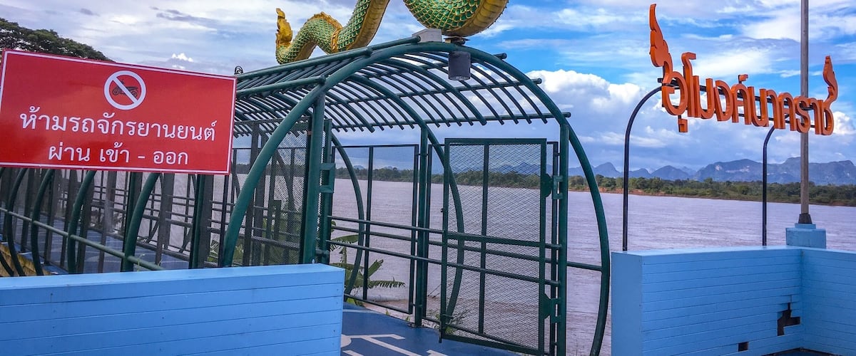 A boat docked by a large dragon statue, a no-motorboat sign, and a sign with Thai script.