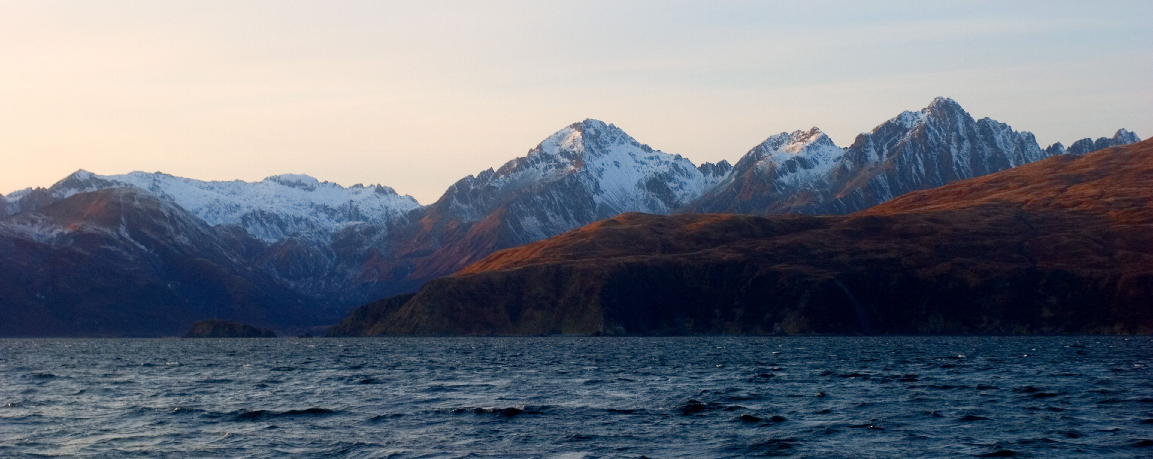 A mountainous landscape with snow-capped peaks and a body of water in the foreground.