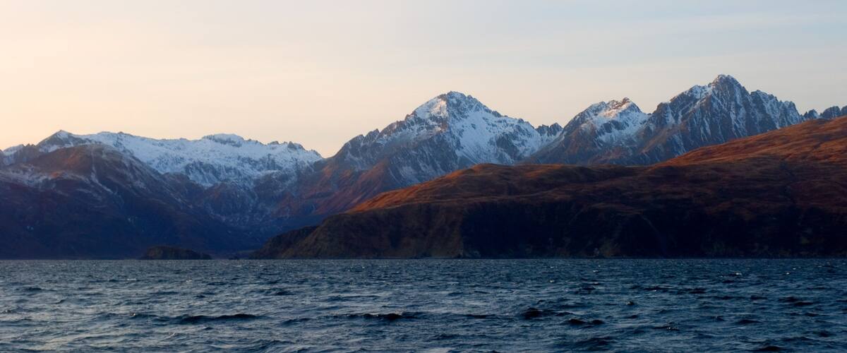 A mountainous landscape with snow-capped peaks and a body of water in the foreground.