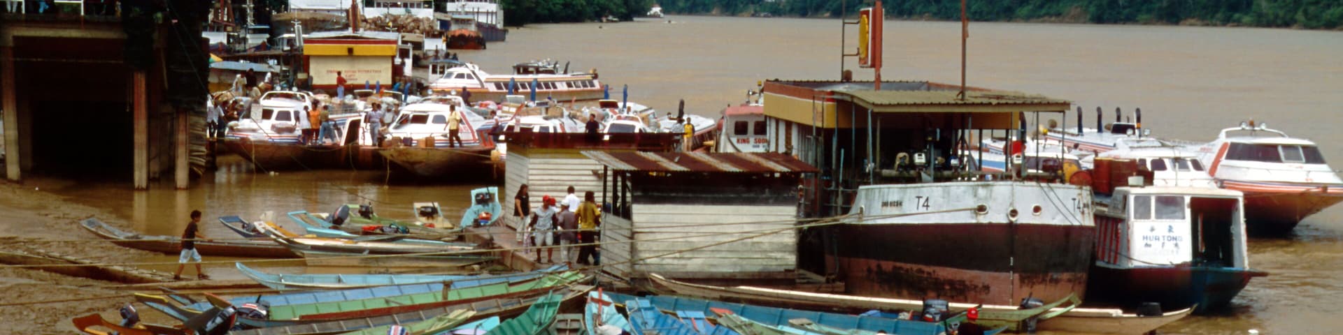 A river with boats docked at a pier, surrounded by greenery.