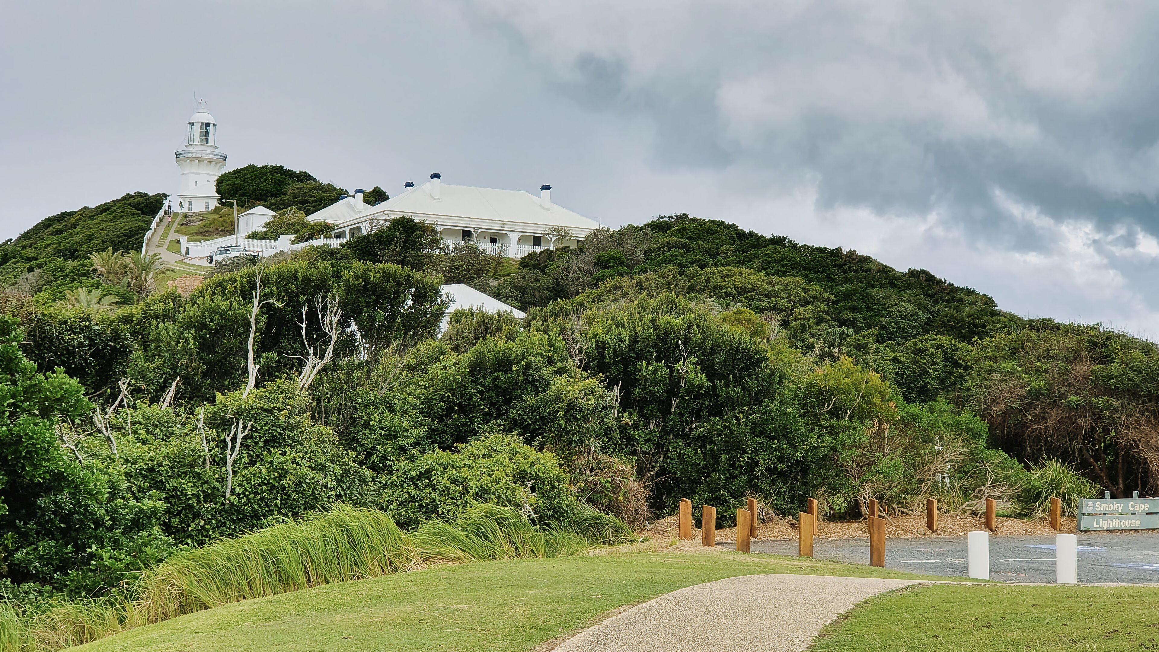A white lighthouse on a hill with lush greenery and a gravel path leading to it.