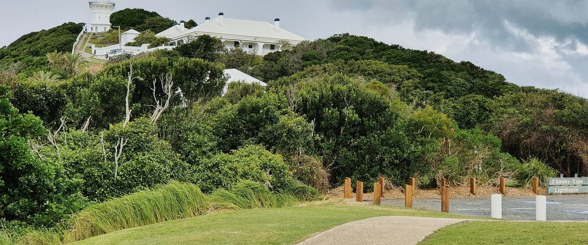 A white lighthouse on a hill with lush greenery and a gravel path leading to it.