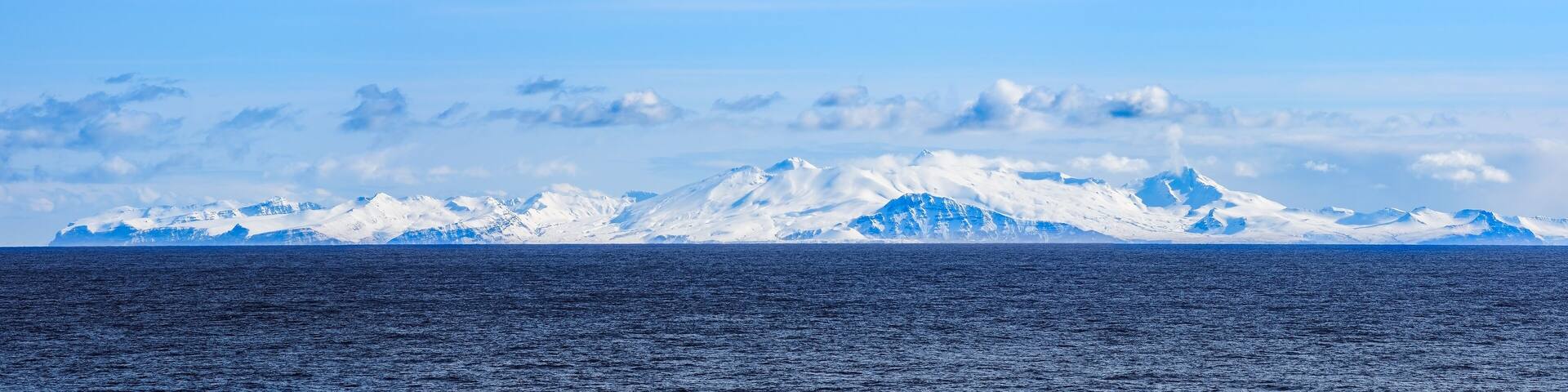 Snow peaks, glaciers and rocks of Aleutian islands in sunny winter day as viewed from ship passing in calm sea
