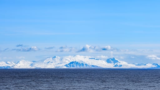 Snow peaks, glaciers and rocks of Aleutian islands in sunny winter day as viewed from ship passing in calm sea