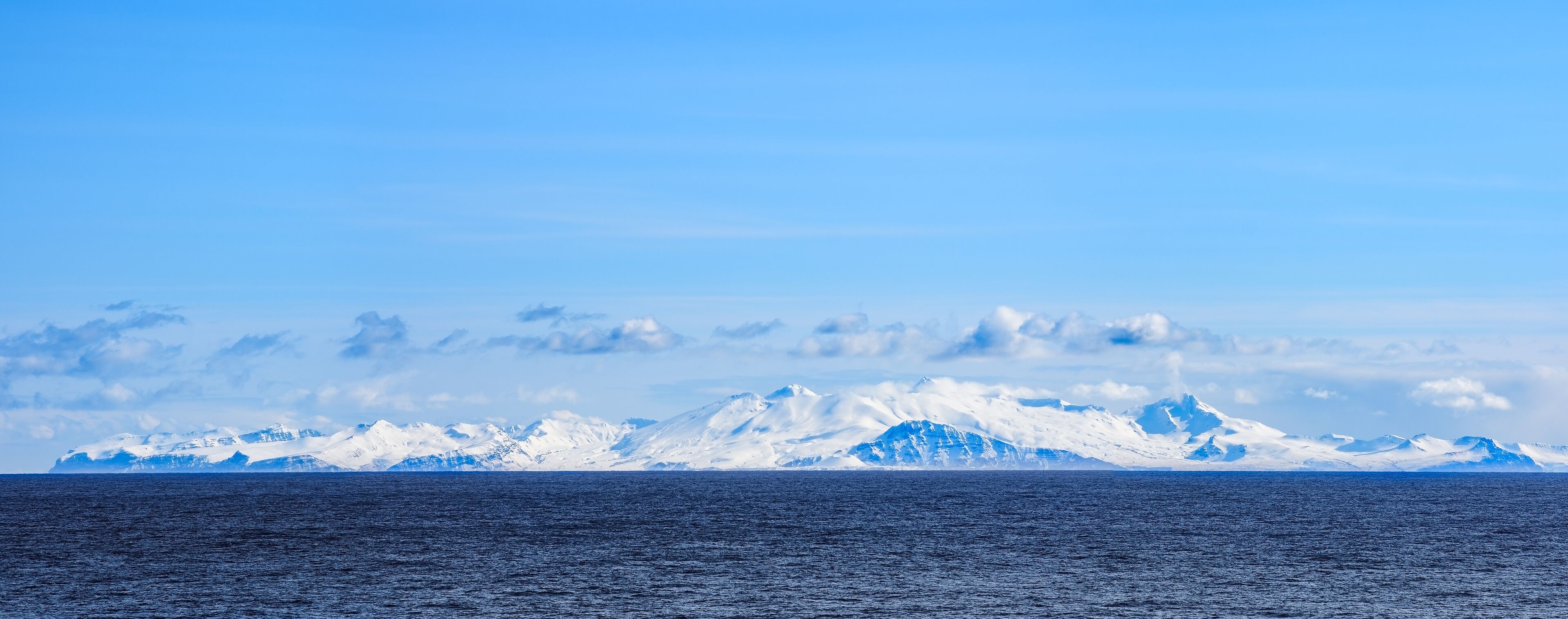 A glacier with a vast ocean in the foreground and a clear sky.