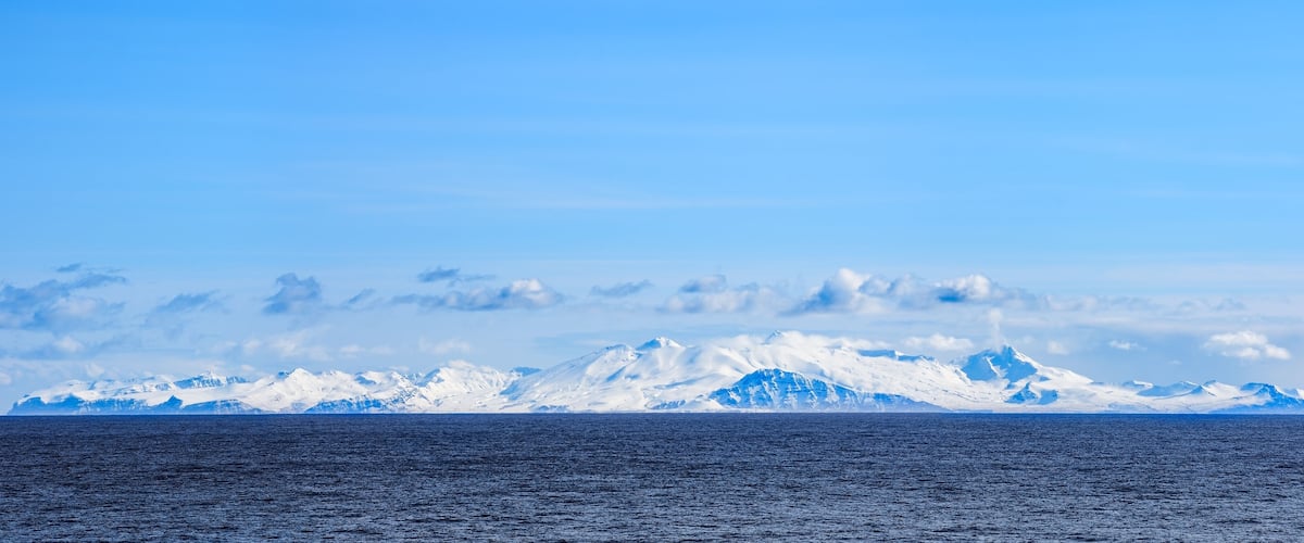 A glacier with a vast ocean in the foreground and a clear sky.