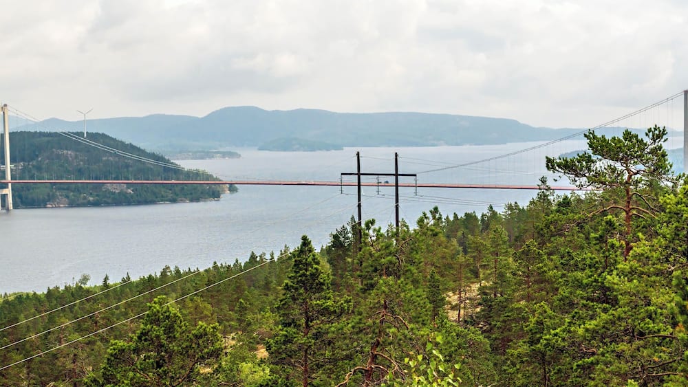 Eine Hängebrücke über einem See mit Bergen im Hintergrund.