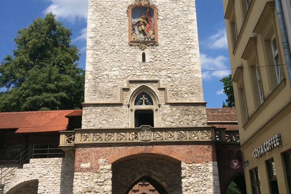 Una torre històrica amb una estàtua, una arcada i un edifici amb un cartell.