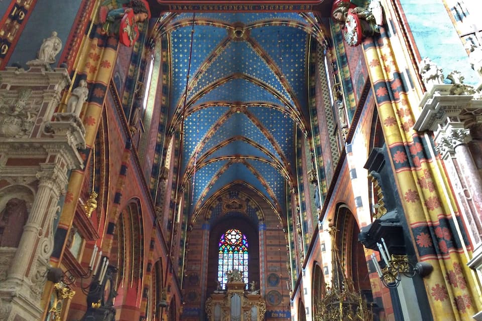 Interior de una catedral con elaboradas bóvedas góticas, vidrieras y una rica decoración.