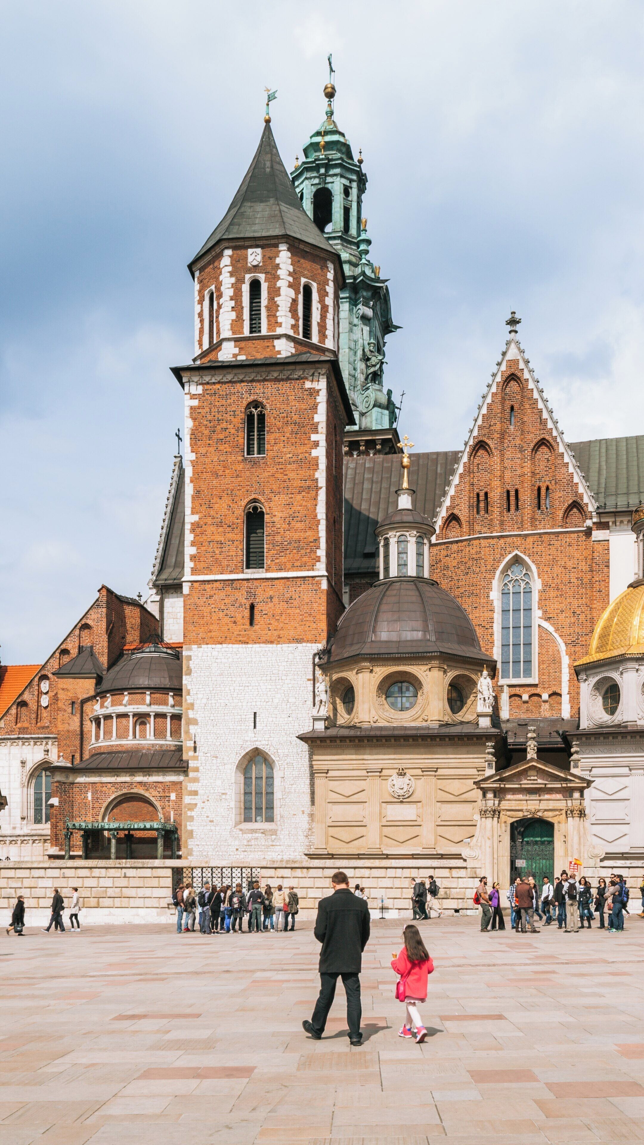 Visitors explore the grandeur of Wawel Cathedral in Kraków, showcasing its architectural beauty against a vibrant sky