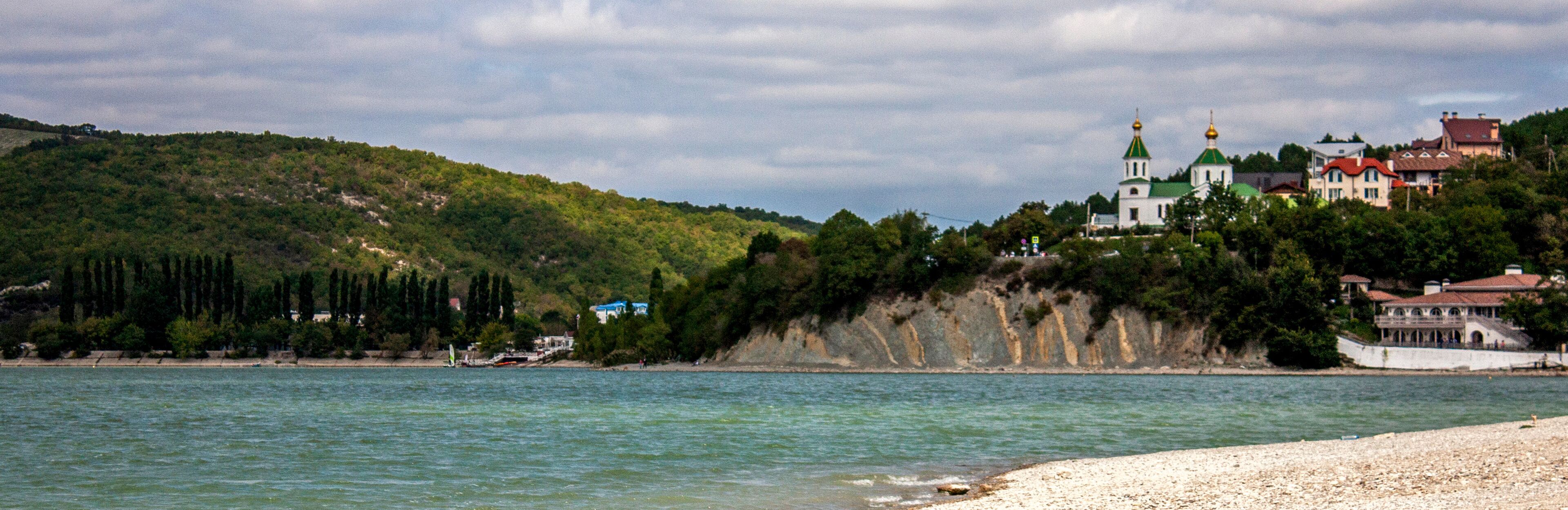 View of the church on the mountain. View of Lake Abrau-Durso from the shore. In the village of Abrau-Durso, on the mountain stands the Church of Blessed Xenia of Petersburg.