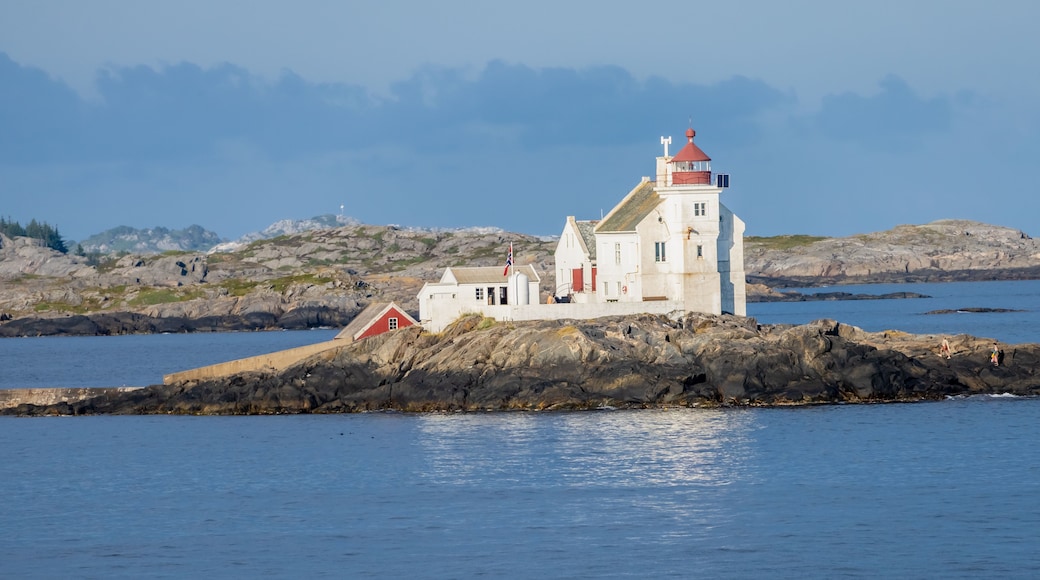 Un phare blanc, surmonté d’un toit rouge, se dresse sur une île rocheuse, entourée d’eaux calmes.