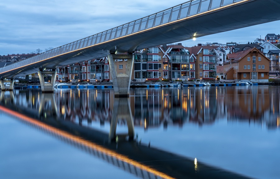 Un puente sobre aguas tranquilas con edificios reflejándose en la superficie.