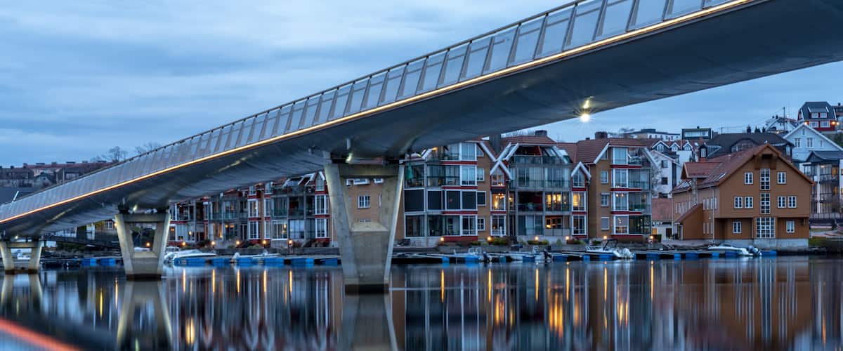 A bridge over calm water with buildings reflecting on the surface.