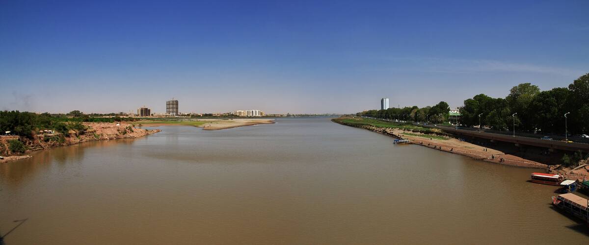 A river with a bridge, a boat, and a cityscape in the distance.