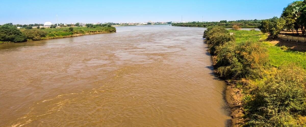 Un río ancho con una orilla cubierta de hierba y un horizonte urbano lejano.