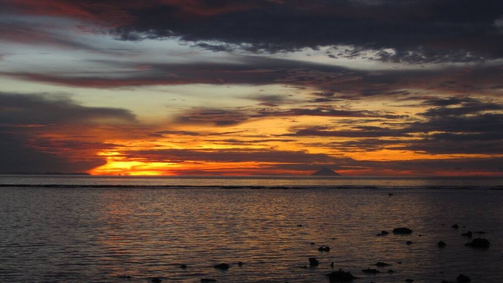 A sunset over a body of water with scattered rocks.