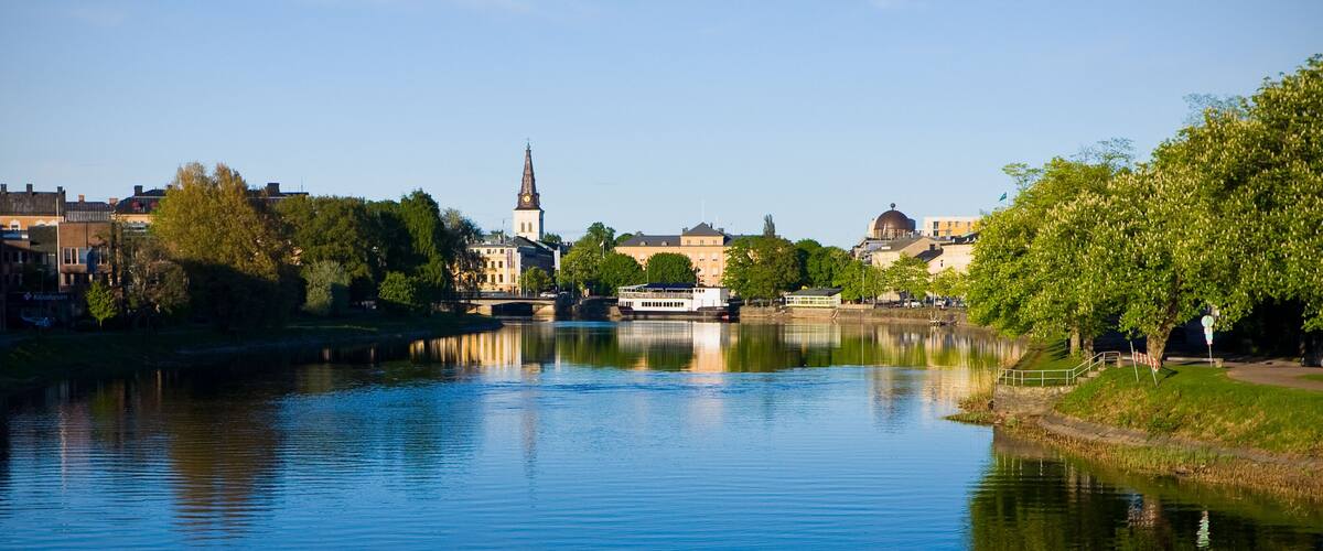 Ein ruhiger Fluss mit einem Boot, einem Kirchturm und Gebäuden am Ufer.