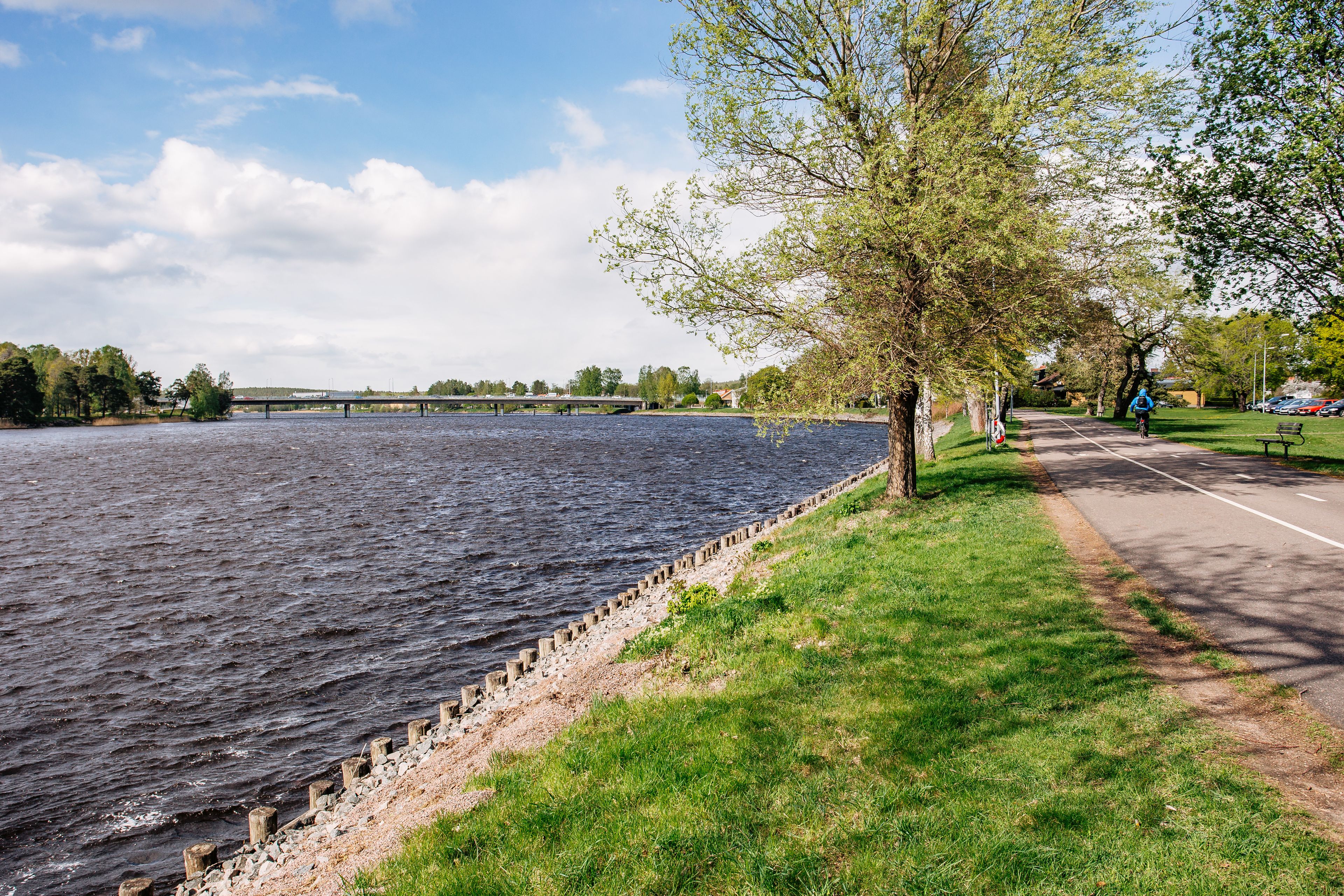 A river with a concrete embankment, a pedestrian path, and a bridge in the distance.