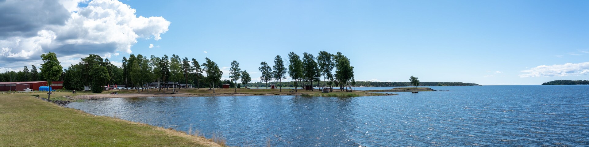 Un lago con una orilla cubierta de hierba, árboles y edificios al fondo.