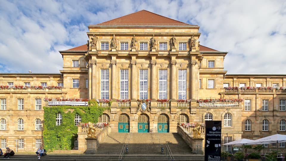 A large historic building with a red-tiled roof, multiple windows, and statues on the facade.