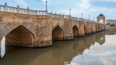 A brick bridge with arched supports over a calm river.