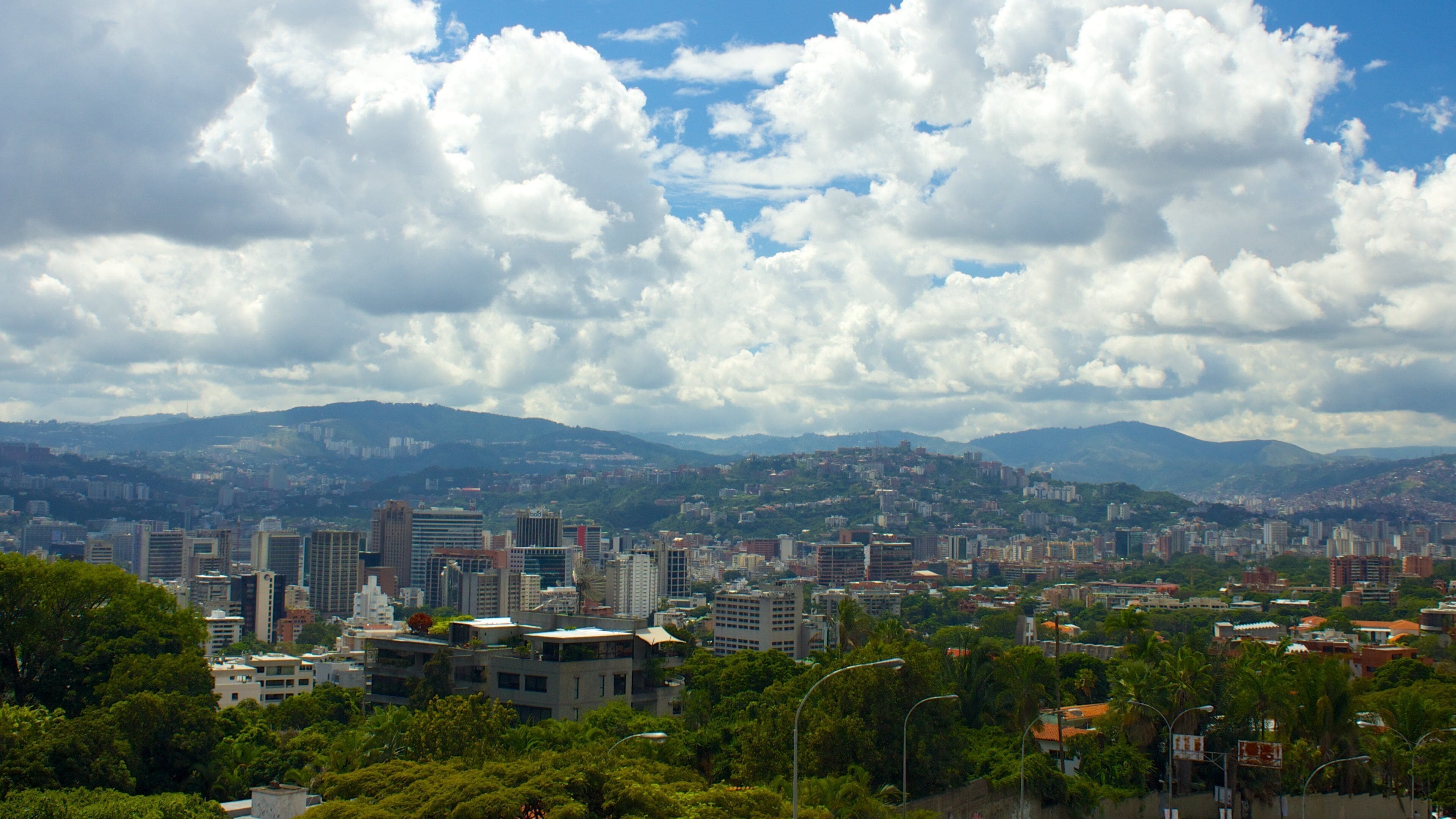 A cityscape with mountains in the background and a partly cloudy sky.