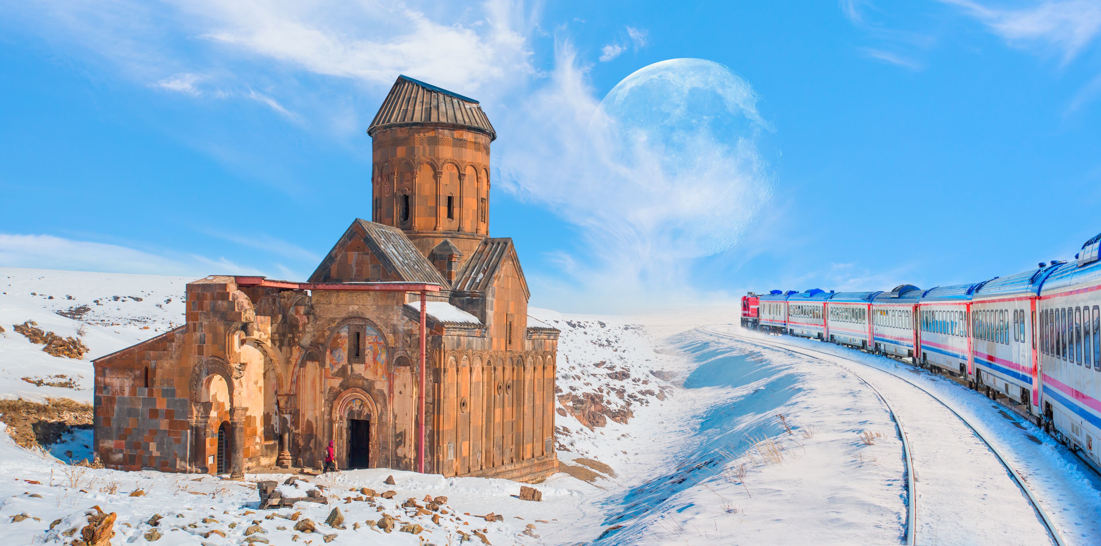 A snow-covered landscape with a historic church and a train track.